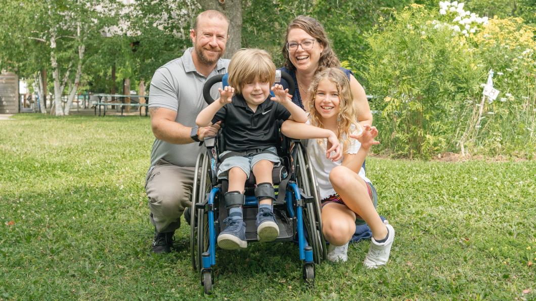Boy outside in wheelchair beside girl with man and woman behind