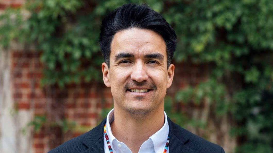 Man with dark hair and colourful necklace