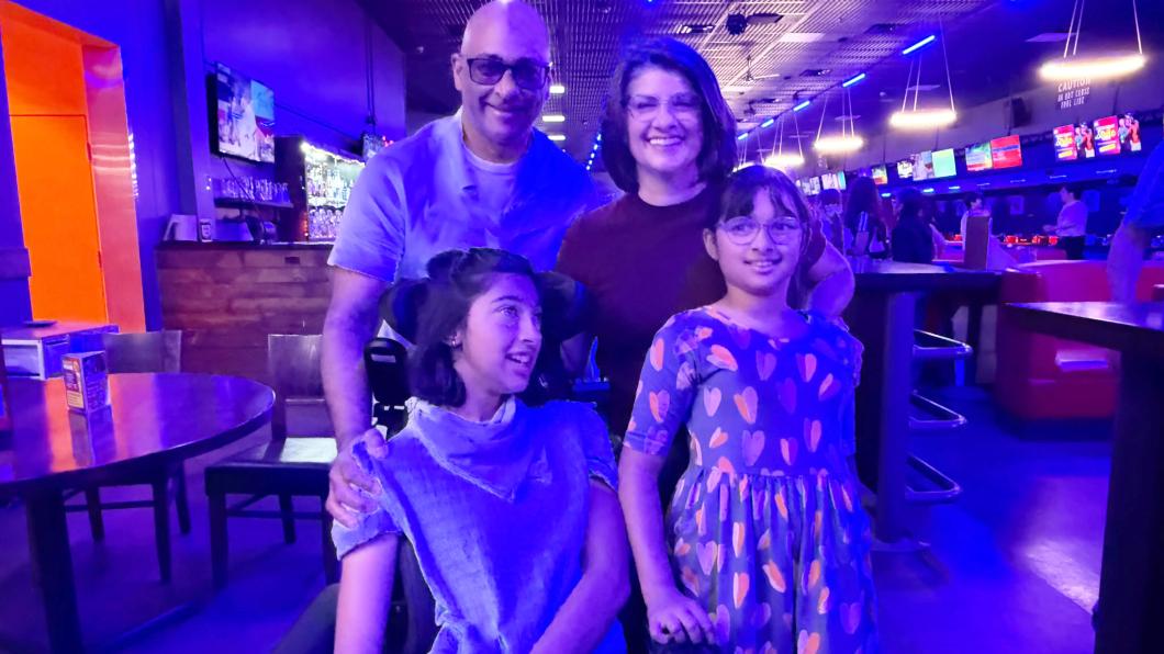 Girl in wheelchair with another girl beside her and man and woman behind in bowling alley