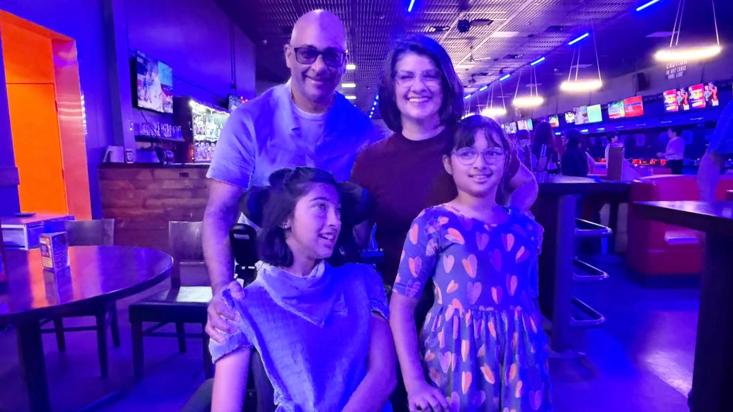 Girl in wheelchair with another girl beside her and man and woman behind in bowling alley