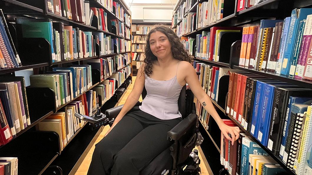A young person who uses a wheelchair in between two library bookshelves