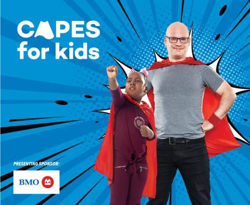 Image of adult man and younger male child posing as superheroes against blue backdrop that says "Capes for Kids"