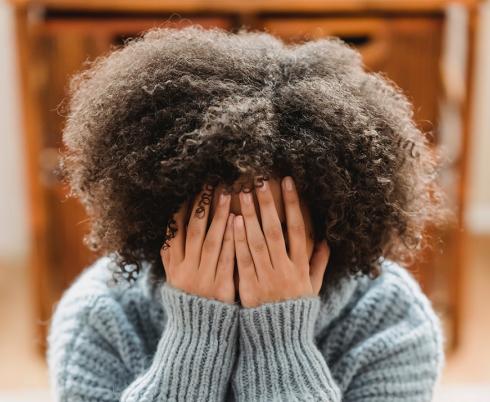 Image of young adult covering their face with their hands, hunched over