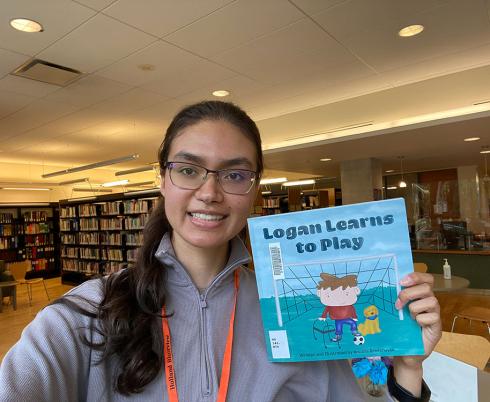 Anusha holding her book: Logan Learns to Play.