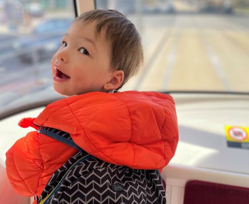 James standing at the front of a streetcar, behind the window, looking over his shoulder