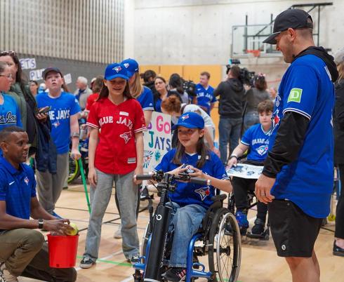 A kid on wheelchair accompany with some adults in a basketball courtyard