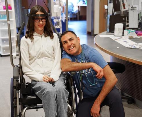An adult with a teenager who is sitting on a wheelchair
