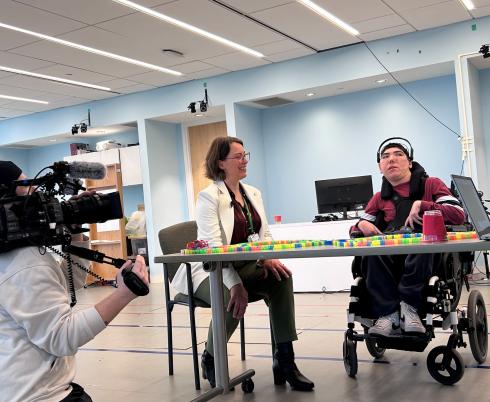 reporter with a camera is filming a clinician and a teen using brain computer interface