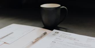 An application form and pen with a mug of tea or coffee in the background