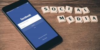 A smart phone displaying the homepage for Facebook on left, scrabble letters spelling Social Media to right of phone