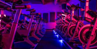 Indoor bicycles lined up in a row with purple and blue light reflecting on them.