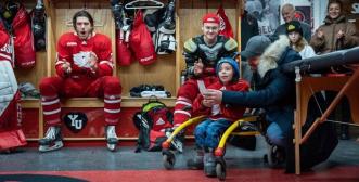 a young boy using a walker, speaking with hockey players in the dressing room.